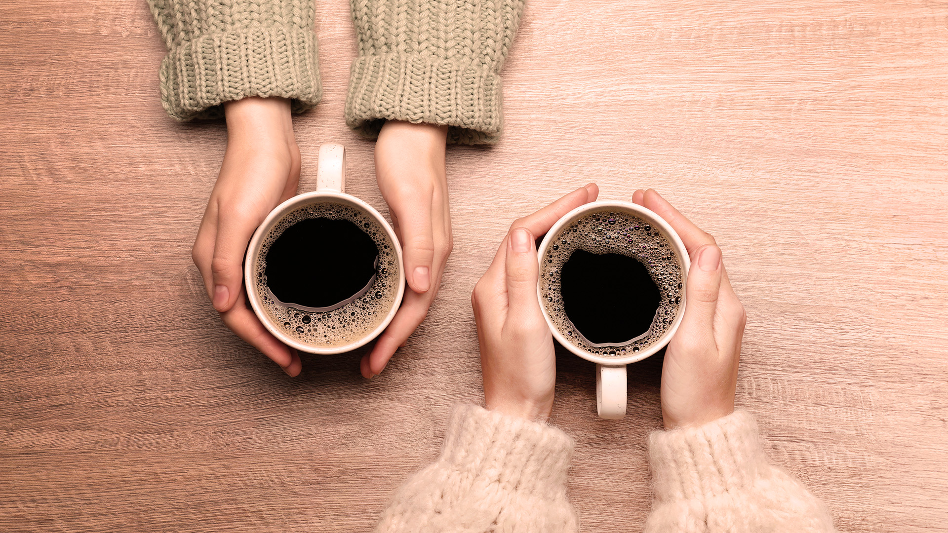 Två par händer som håller om varsin kopp med kaffe